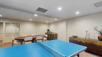 A room with a ping pong table, a dining table with chairs, a kitchenette, and a cabinet with decorative items.