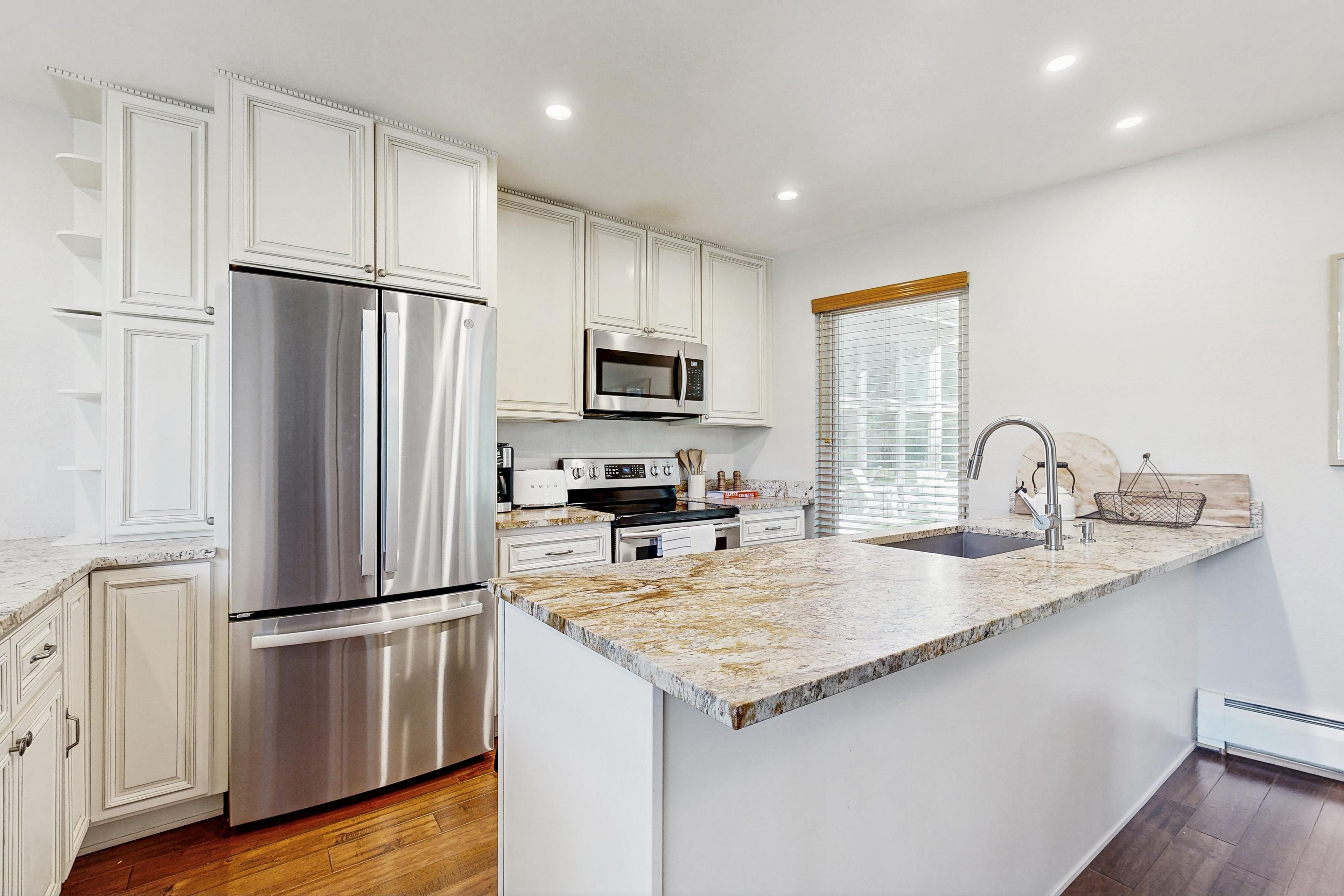 A modern kitchen with white cabinetry, stainless steel appliances, and a marble countertop.