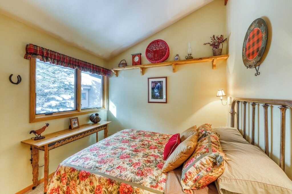 Un dormitorio con cama, ventana, repisa con adornos y una lámpara fijada a la pared.
