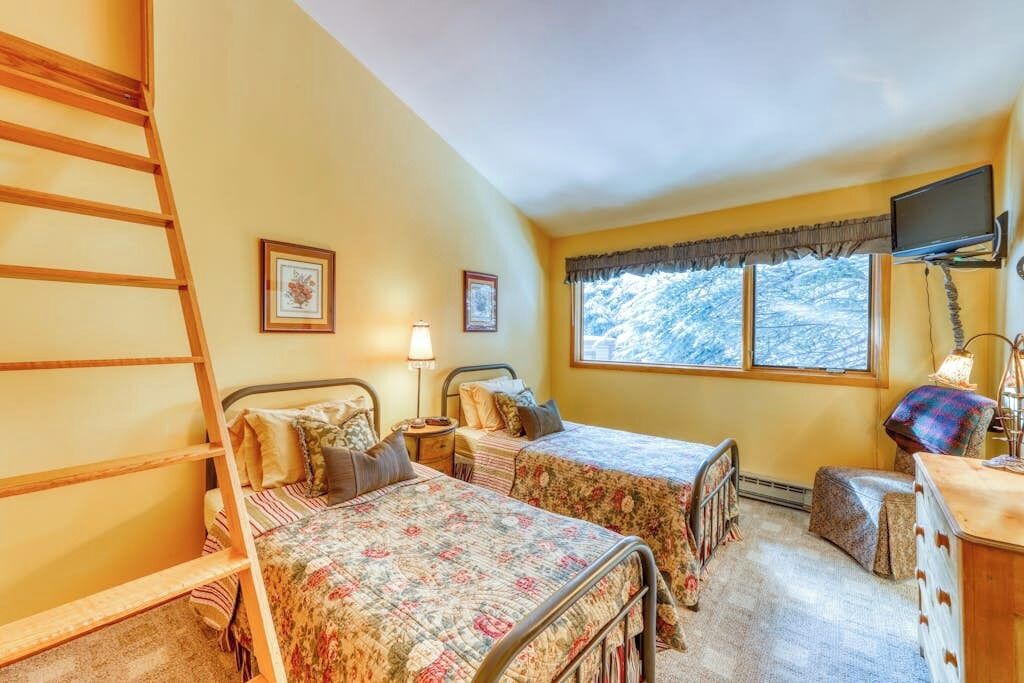 A bedroom with two beds, a ladder, a TV, and a window with a view.