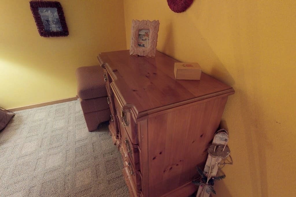 Un aparador de madera con cajones y un espejo, una caja pequeña en la parte superior y un par de zapatos colgados en la pared.