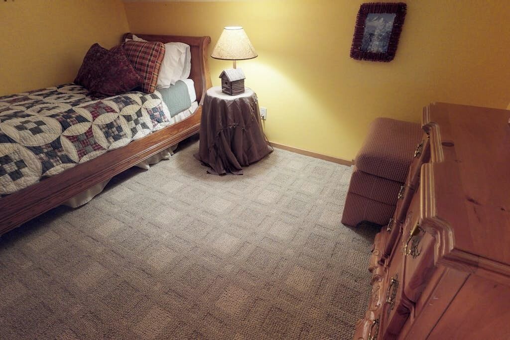 A bedroom with a bed, a nightstand with a lamp, a dresser, and a wall-mounted picture frame.