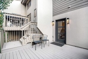 Eine Terrasse mit zwei Stühlen, einer Treppe und einer Tür mit einer Lampe.