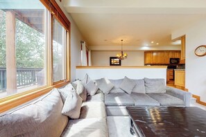 Ein Wohnzimmer mit großem Fenster, einer Couch und einer Küchenzeile im Hintergrund.