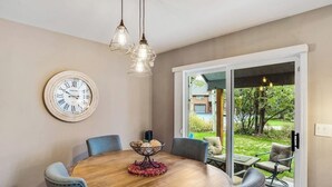 Ruokailutilassa on pyöreä pöytä, tuoleja, kello ja näkymä puutarhaan, joka avautuu liukuovien kautta.