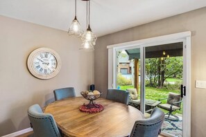 Ein Essbereich mit einem runden Tisch, Stühlen, einer Uhr und Blick auf einen Garten durch eine Schiebetür.