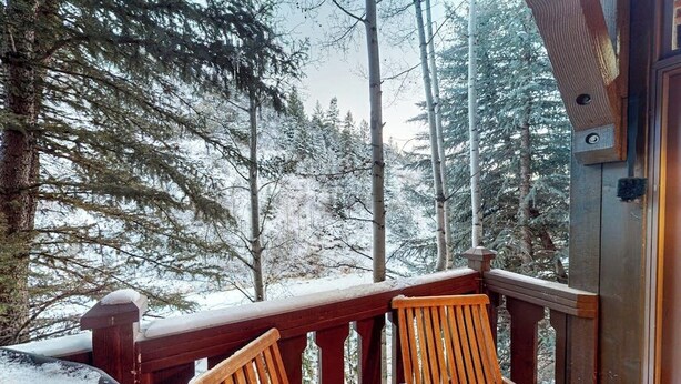 A wooden deck with chairs, surrounded by snow-covered trees.