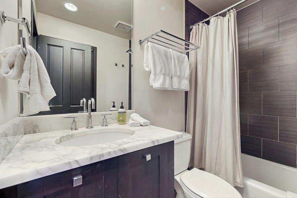 A bathroom with a marble sink, dark wooden cabinets, a white toilet, and a shower curtain.
