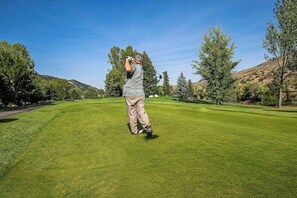 Eine Person auf einem Golfplatz bei blauem Himmel.