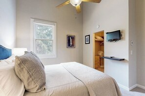 Ein Schlafzimmer mit Bett, Deckenventilator, Wandfernseher, Fenster und einem Schrank mit Spiegel.