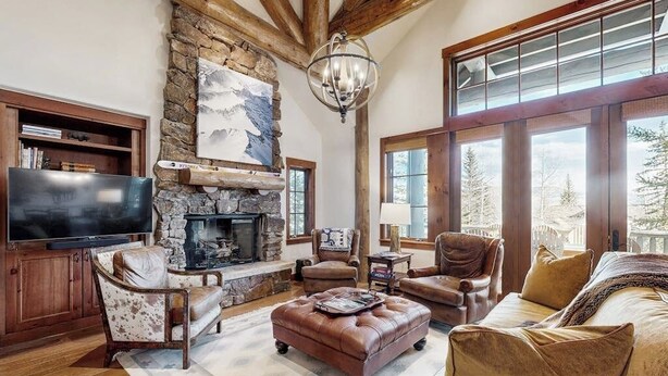 A cozy living room with a stone fireplace, leather furniture, and large windows offering a view of trees. - Ski-in ski-out home w/ large kitchen, hot tub & great location (Avon)