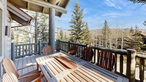 A wooden deck with a table and chairs, surrounded by a railing, overlooking a forested area. - Ski-in ski-out home w/ large kitchen, hot tub & great location (Avon)