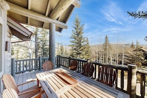 Eine Holzterrasse mit Tisch und Stühlen, umgeben von einem Geländer, mit Blick auf eine bewaldete Landschaft.