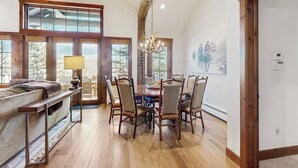 A dining area with a wooden table and chairs, large windows, and a chandelier. - Ski-in ski-out home w/ large kitchen, hot tub & great location (Avon)