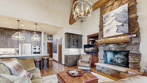 A spacious living area with a fireplace, leather furniture, and a kitchen in the background. - Ski-in ski-out home w/ large kitchen, hot tub & great location (Avon)
