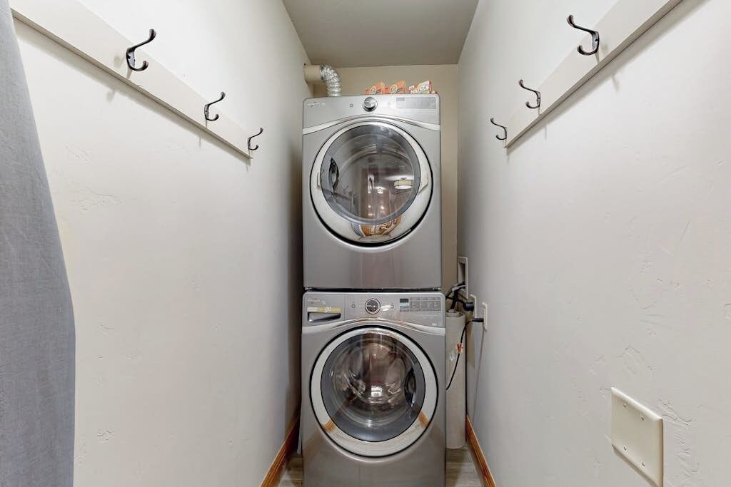 A laundry room with two stacked front-loading washing machines, a wall-mounted heater, and hooks for hanging items.