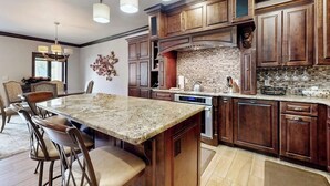 Una cocina con armarios de madera oscura, una isla de granito e iluminación colgante.