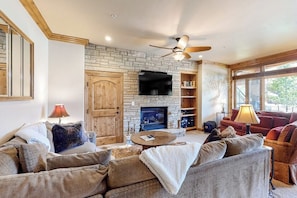 A living room with a stone fireplace, a ceiling fan, and a television mounted on the wall. - Ski-In/Ski-Out Villa w/ Fireplace, High-Speed WiFi & Shared Hot Tub, Pool, & W/D (Vail)