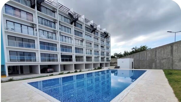 Un edificio moderno con piscina, varios balcones y cielo despejado.