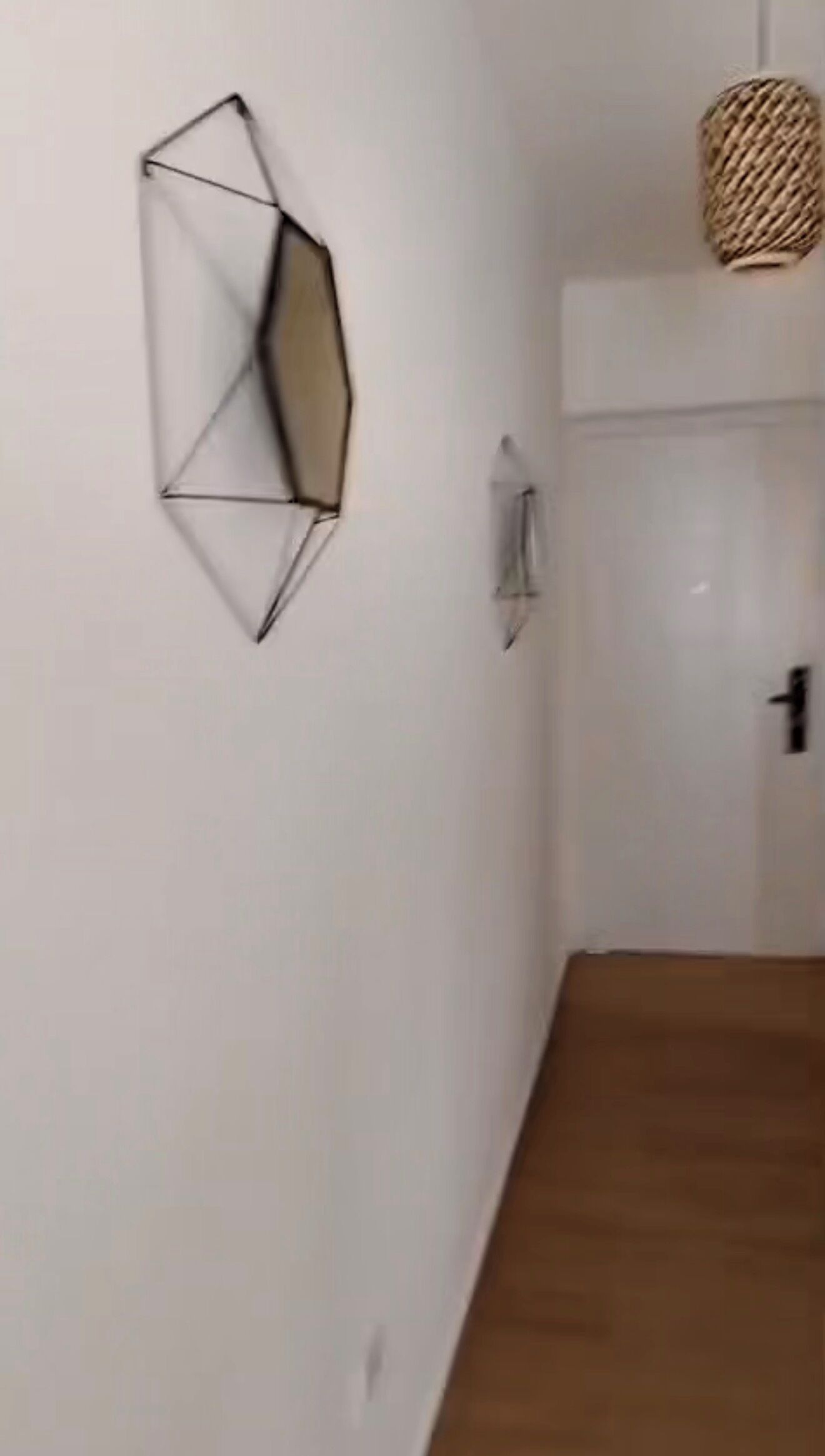 En gang med geometrisk vægpynt, en hængende lampe og en dør med et nummer.