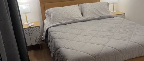 A neatly made bed with a wooden headboard, two bedside tables with lamps, and a wall-mounted air conditioner.