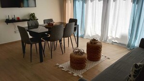 Un comedor con mesa y sillas, un televisor montado en la pared y una ventana con cortinas.