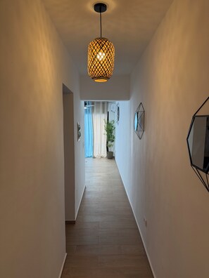 Ein Flur mit einer gemusterten Pendelleuchte, einer Topfpflanze und geometrischer Wandkunst.
