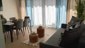 Una sala de estar con un sofá, una mesa de comedor con sillas y dos otomanas de mimbre.