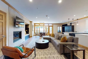 Ein modernes Wohnzimmer mit Sofa, Couchtisch und Fernseher. Ein Kamin, ein Essbereich und eine Küche sind ebenfalls zu sehen.