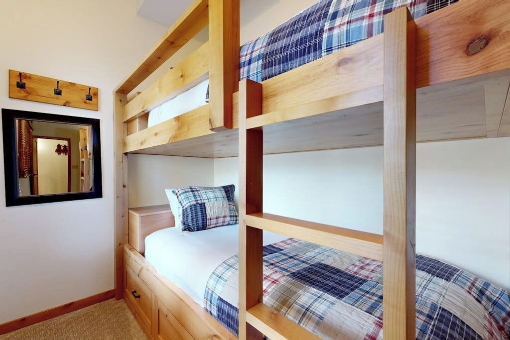 Une chambre avec un lit superposé, un miroir, des meubles en bois et une couvre-lit à carreaux.