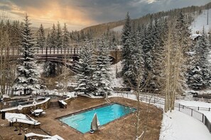 Ein Poolbereich mit einer Holzbrücke, umgeben von schneebedeckten Bäumen und einer Bergkulisse.