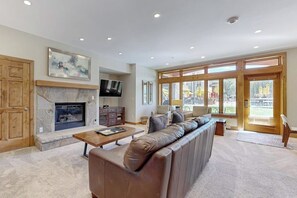 A living room with a fireplace, a television, a sofa, and large windows. - Ski-in/ski-out home w/ high-speed WiFi, fireplace & shared pool/hot tubs/laundry (Vail)