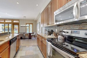 A modern kitchen with wooden cabinets, stainless steel appliances, and a stone backsplash. - Ski-in/ski-out home w/ high-speed WiFi, fireplace & shared pool/hot tubs/laundry (Vail)