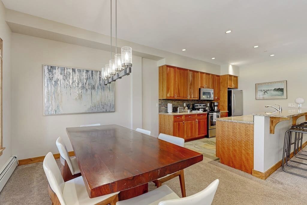 Une cuisine moderne avec des meubles en bois, un îlot central et un coin repas comprenant une table en bois et des chaises blanches.