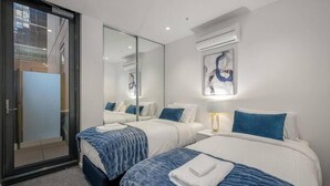 Ein Hotelzimmer mit zwei Betten, einer Schiebetür, einer Wand-Klimaanlage und einem großen Spiegel, der das Zimmer reflektiert.