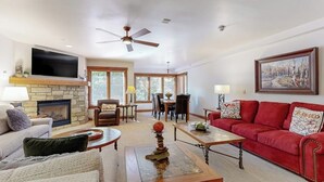 A living room with a fireplace, a red sofa, a television, and a ceiling fan. - Winter Villa in Ski-In/Ski-Out Complex w/Free WiFi & Shared Pool, Hot Tubs, W/D (Vail)