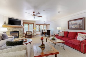 A living room with a fireplace, a red sofa, a television, and a ceiling fan. - Winter Villa in Ski-In/Ski-Out Complex w/Free WiFi & Shared Pool, Hot Tubs, W/D (Vail)