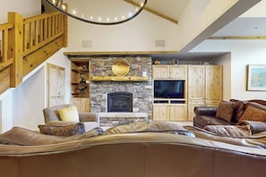 Ein Wohnzimmer mit Kamin aus Stein, Holzschränken, einem Fernseher und einer Treppe.