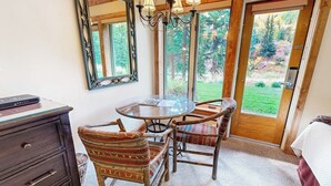 A room with a round glass table, two patterned chairs, a wooden dresser, a large mirror, and a door leading to a garden. - Ski-in/out, mountain view studio w/ fast WiFi & shared pool, hot tubs, laundry (Vail)