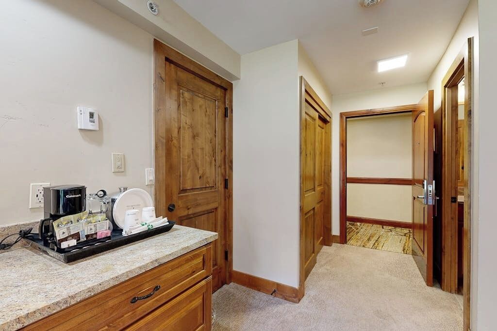 Camera d'albergo con angolo cottura, armadio in legno, pavimento in moquette e una porta che conduce a un'altra stanza.