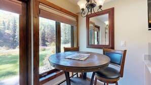 Un coin repas avec une table ronde, deux chaises, un lustre et un grand miroir au mur.