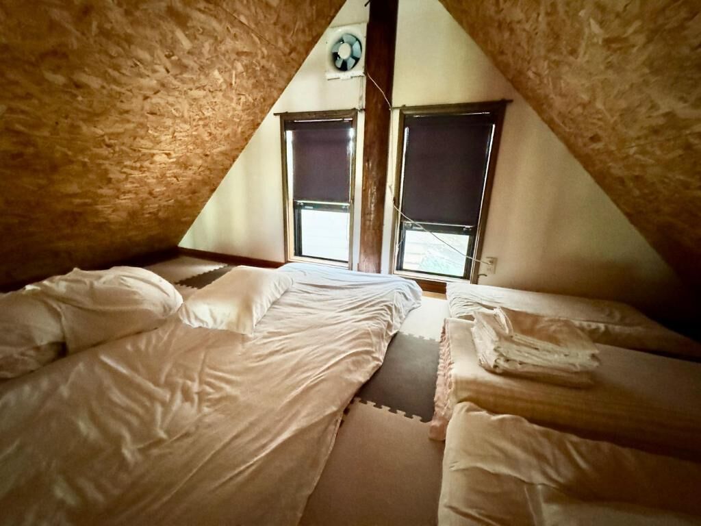 A triangular attic room with two beds, a ceiling fan, and two windows.