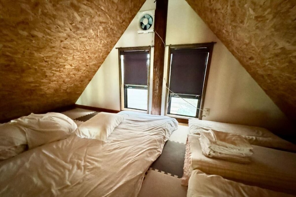 A triangular attic room with two beds, a ceiling fan, and two windows.