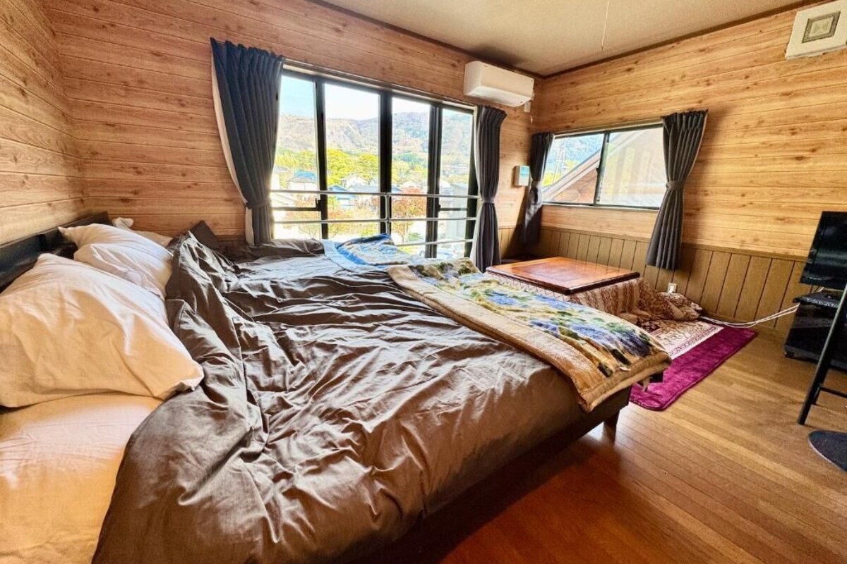 A wooden cabin room with a bed, a small table, and a window with curtains.