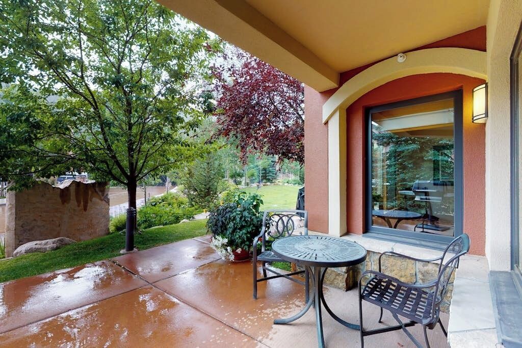 An outdoor patio with a table and chairs, a potted plant, and a view of the surrounding greenery.