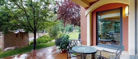 An outdoor patio with a table and chairs, a potted plant, and a view of the surrounding greenery.
