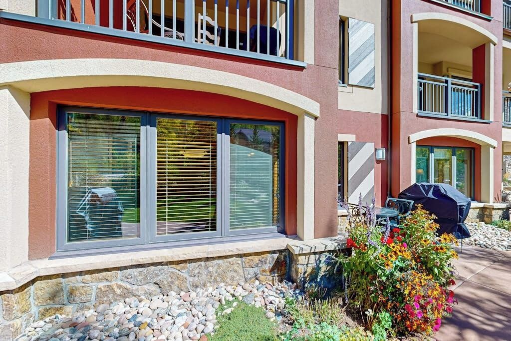 A multi-story building with balconies, large windows, and a garden area with flowers and a grill.
