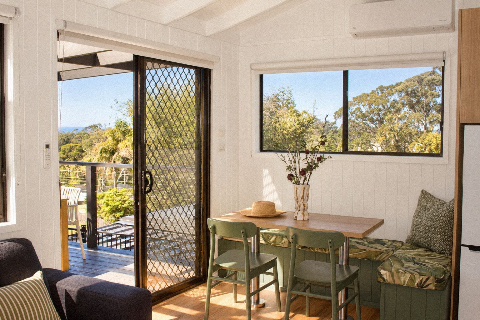 A room with a sliding glass door leading to an outdoor area, a table with chairs, and a view of trees through the window.