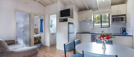 A modern kitchen with white cabinets, a microwave, and a dining area with a round table and chairs.