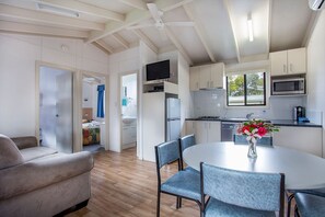 Een moderne keuken met witte kasten, een magnetron en een eethoek met een ronde tafel en stoelen.